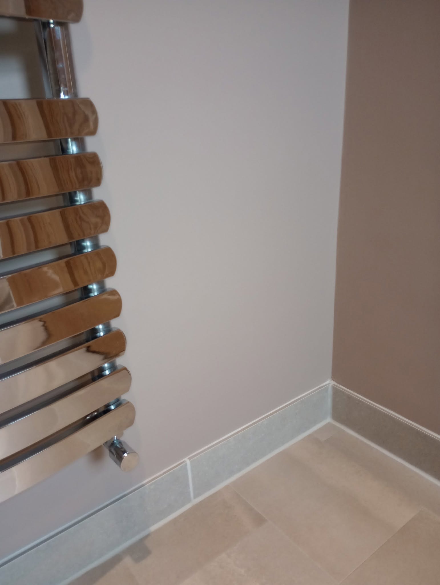 Bathroom wall in pale grey beside a chrome and wood towel rail