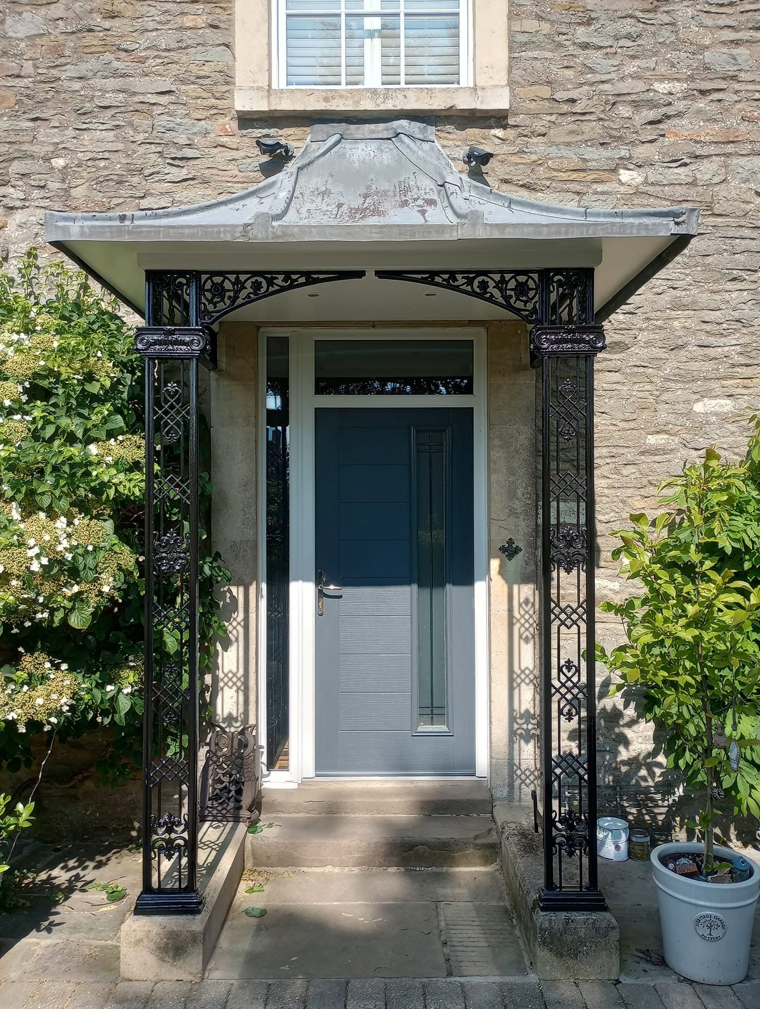 Grey front door under an ornate black iron porch on a stone house