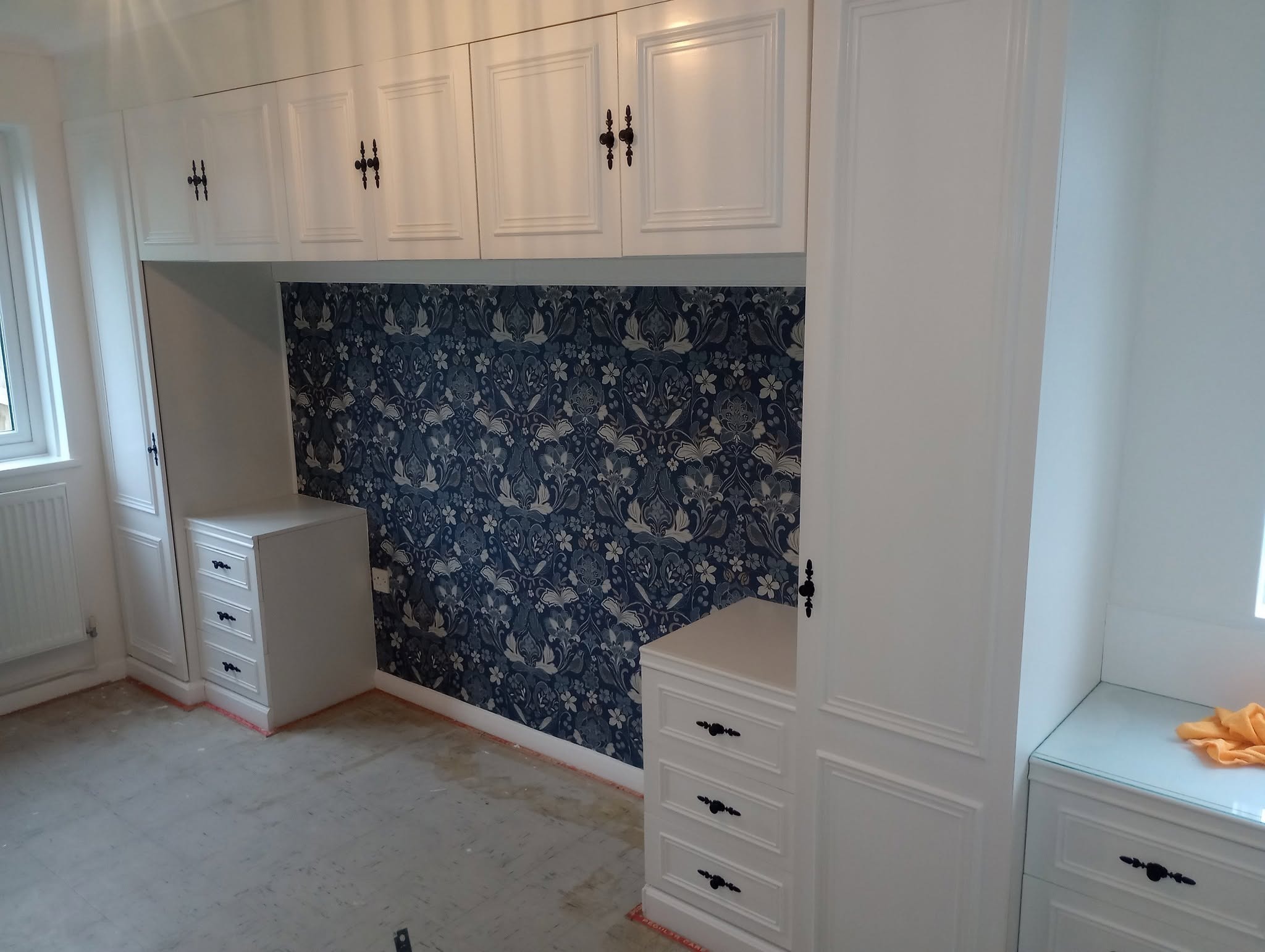 Built-in wardrobes and drawers painted white beside a patterned wall